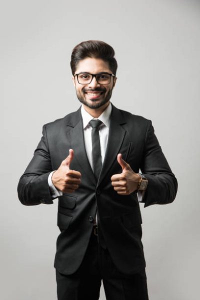 Indian Bearded Male businessman celebrating success with thumbs up or raising fist while standing isolated over black background